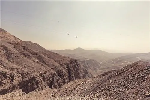 Два зип-лайнера пролетают над каньоном на проводах на большой высоте над красным скалистым пейзажем