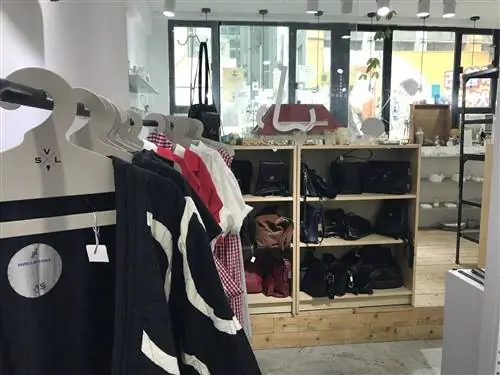 Выбор одежды на вешалках на переднем плане и полка с сумками и кошельками на заднем плане