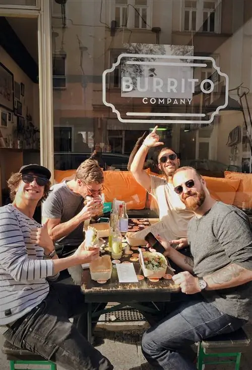 Группа мужчин, сидящих за столом в су возле компании Burrito. На столе смесь мексиканской кухни.