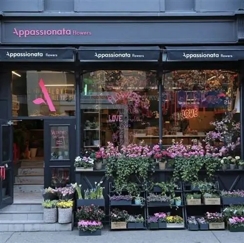 Фасад магазина Appassionata Flowers. Перед большими окнами и черным фасадом магазина стоят ряды цветных цветов.