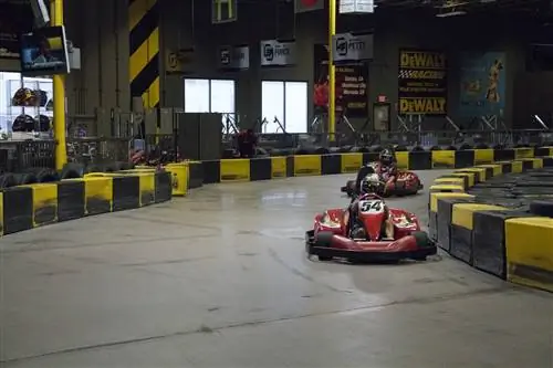 Желтые и черные барьеры ограничивают широкое пространство извилистой трассы для картинга, где гонщики на красных автомобилях мчатся за угол.