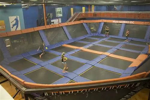 Показана большая арена, состоящая из мягких стен и нескольких батутов в качестве пола, а люди стоят внутри и играют в вышибалы.