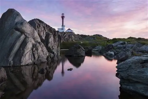 Скалистая береговая линия на восходе солнца с пурпурно-розовым небом, отражающимся в воде, и маяк на мысе Форчу на расстоянии