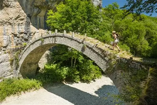 Женщина идет по мосту Контодимос (Гефири Лазариди), узкому одноарочному каменному мосту через высохшее русло реки недалеко от Кипоя.