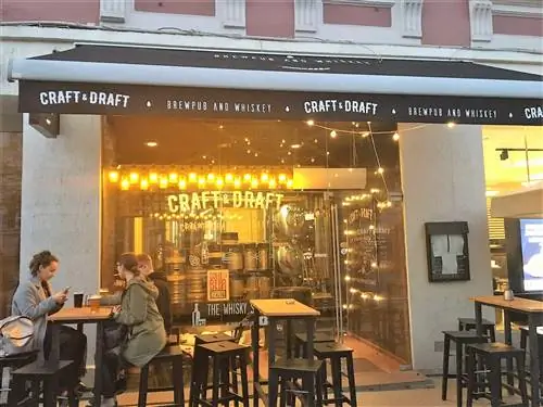 Три посетителя сидят за высокими столиками и пьют пиво возле Craft & Draft.