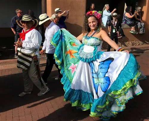 Женщина улыбается в камеру, прогуливаясь по улице. На ней красивое платье с замысловатым узором, которое она с гордостью демонстрирует на камеру.