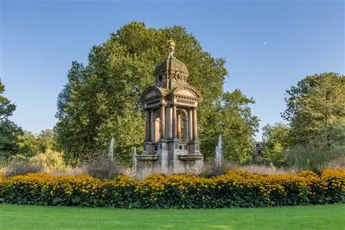 Отдельно стоящий каменный памятник в центре фонтана в окружении цветов.