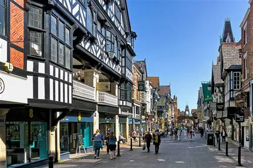 Вид на главную улицу в центре Честера, Чешир, Великобритания. Магазины можно увидеть по обеим сторонам дороги, а людей можно увидеть прогуливающимися и сидящими на скамейках. Ряды магазинов верхнего уровня изображены слева.