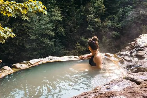 Женщина сидит в горячем источнике в окружении леса