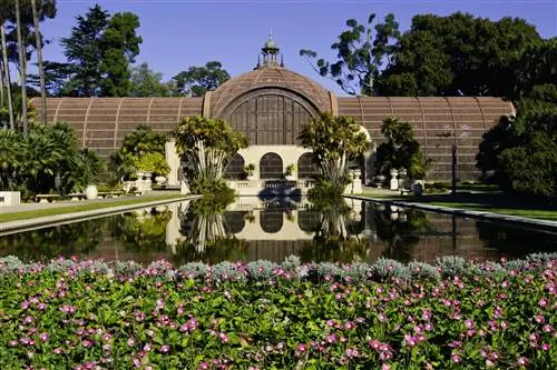Ботаническое здание в парке Бальбоа в Сан-Диего отражается в озере, окруженном цветами.