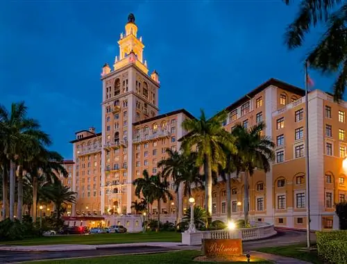 Желтый отель Biltmore в Майами подсвечивается ночью пальмами в палисаднике.