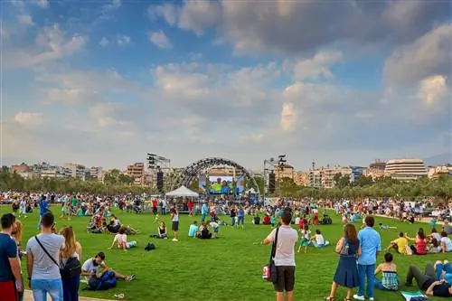 Толпы людей сидят на траве в парке Ставроса Ниархоса и наслаждаются концертом на солнце.