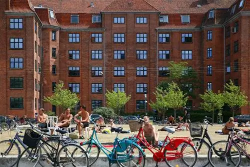 Ряд припаркованных велосипедов закрывает вид на людей, сидящих на пляже и загорающих.