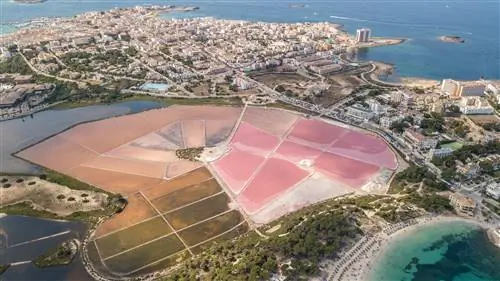 Розовые солончаки расположены рядом с бирюзовой лагуной и голубыми морскими водами в окружении белого городского пейзажа в Колония-де-Сант-Жорди в Испании.