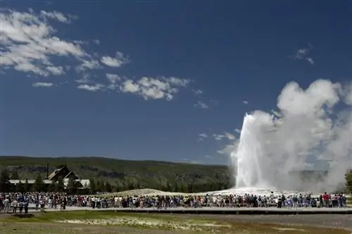 Толпы людей окружают гейзер Old Faithful в летний день во время туристического сезона в Йеллоустонском национальном парке.