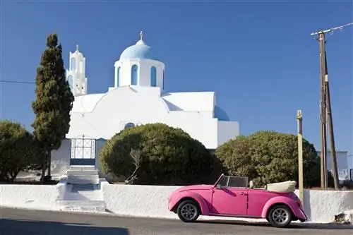 Розовый Volkswagen Beetle перед часовней на Санторини, Греция
