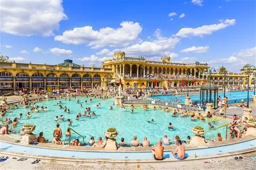 Люди сидят в полукруглом бассейне за желтым зданием с арками в солнечный день в Будапеште, Венгрия.
