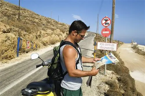 Мужчина стоит на обочине дороги рядом с мотоциклом и смотрит на карту в Санторини, Греция.