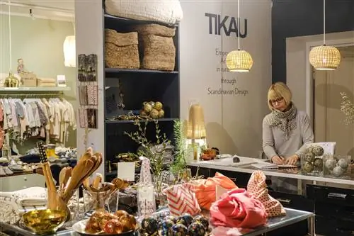 Продавец-консультант стоит за прилавком магазина Tikau в Хельсинки, на переднем плане выставлены изделия ручной работы.