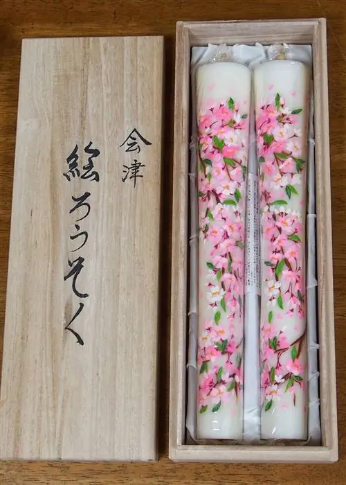 Две свечи Aizu Erōsoku, тонко расписанные розовыми цветами, представлены в деревянной коробке в студии Yamada Shōten.