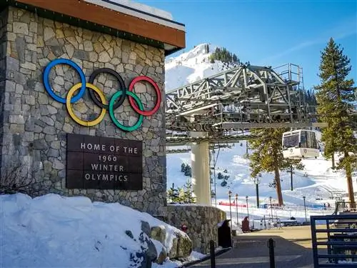 Фото знака курорта с олимпийскими кольцами на территории базы и кресельной канатной дорогой на заднем плане.