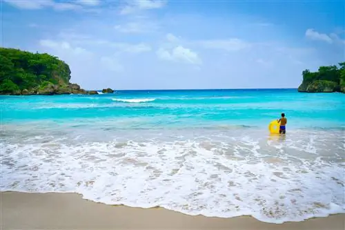 Мужчина с желтым надувным пончиком стоит по колено в воде на пляже Бостон-Бей на Ямайке.