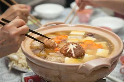 Люди делят набэ с бульоном и зимними овощами, используя палочки для еды.