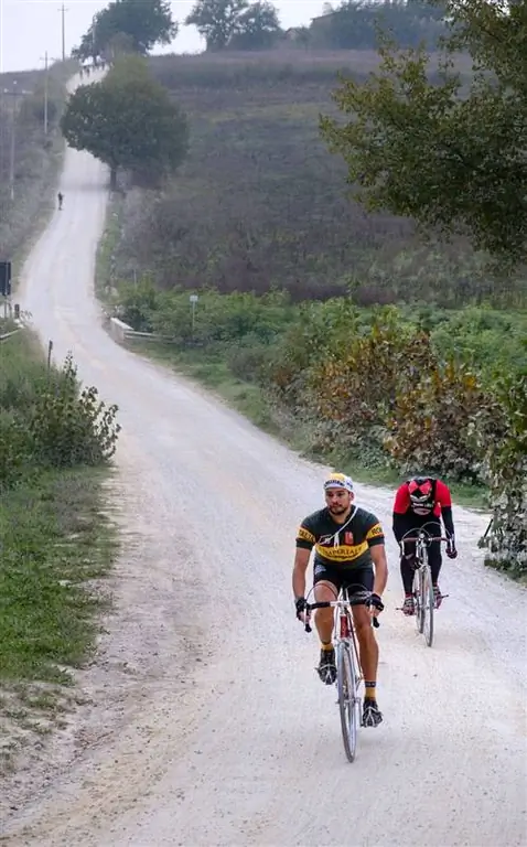 Два велосипедиста-мужчины едут в гору по одной из проселочных дорог strade bianche