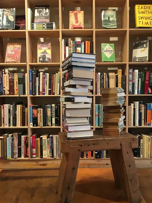 стопка книг лежит на деревянной скамейке перед заполненными книжными полками