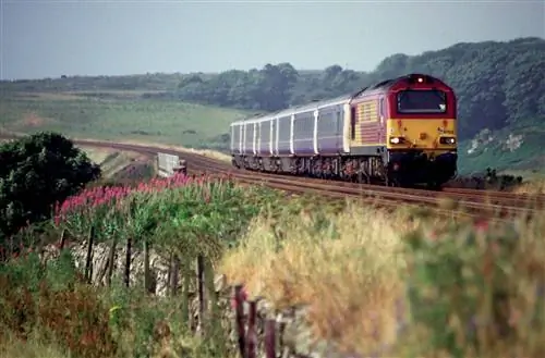 Caledonian Sleeper мчится по участку пути в Шотландии с широкими зелеными полями, расположенными по обе стороны пути.