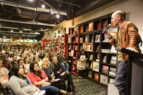автор мужского пола, держащий микрофон, говорит с аудиторией в книжном магазине