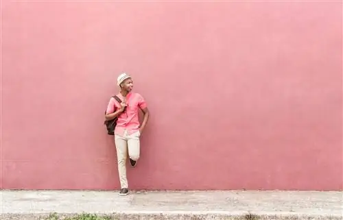 Черный мужчина с рюкзаком и белой шляпой стоит перед красочной розовой стеной в Гондурасе.