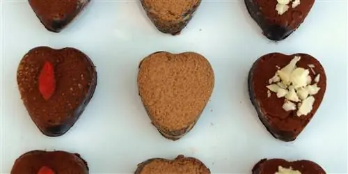 Шоколадные десерты в форме сердца выложены аккуратно рядами. Некоторые посыпаны рублеными орехами, а другие кусочком малины. Шоколадные десерты в форме сердца выложены аккуратно рядами. Некоторые посыпаны рублеными орехами, а другие кусочком малины.