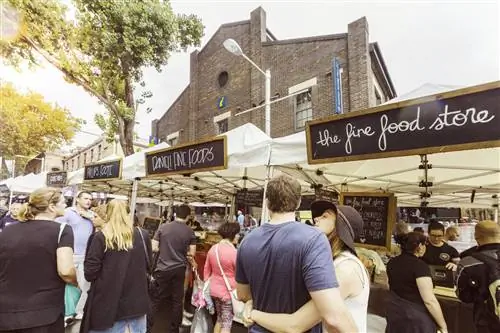 Люди толпятся перед прилавками с едой из белой ткани, названия которых написаны на доске. Пара обнимается перед прилавком, мило.