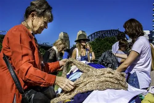 Женщина рассматривает шерстяной джемпер на рынке Киррибилли перед Сиднейским мостом Харбор-Бридж и прекрасным голубым небом.