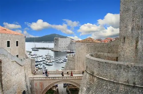 Люди идут по каменному мосту в Дубровнике с гаванью за его пределами