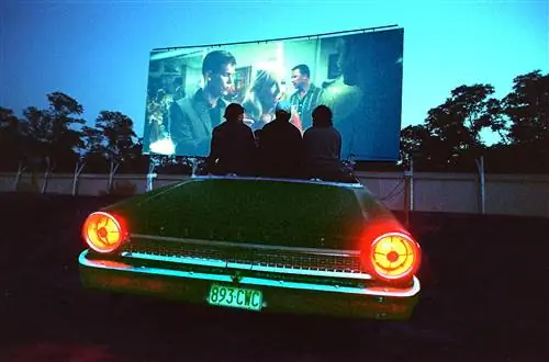 Трое людей сидят на краю машины с видом сверху и смотрят фильм в Wellfleet Drive-In в Кейп-Код, штат Массачусетс.