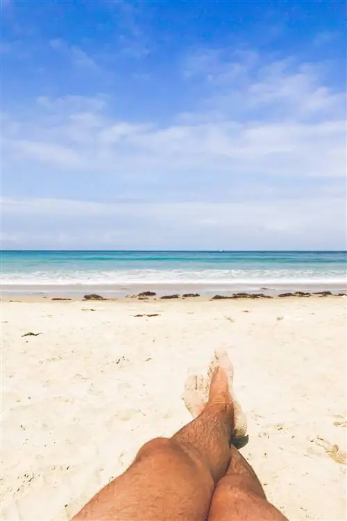 Мужские ноги расслабляются на нудистском пляже Торимбии, муниципалитет Льянес, к северу от Испании.