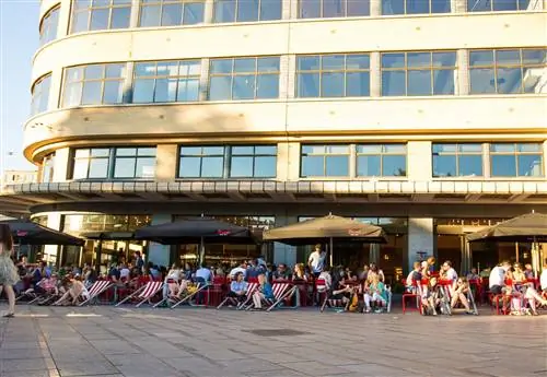 Посетители Café Belga ловят последние лучи полуденного солнца в своих ярких шезлонгах.