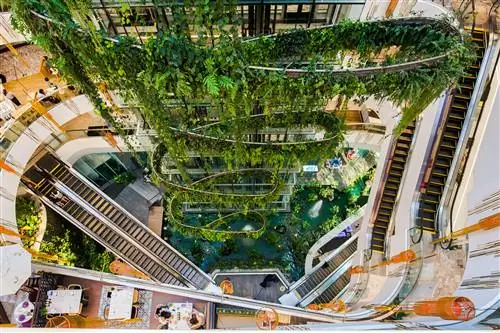 Квартал Helix в торговом центре Emquartier в Таиланде, вид с верхнего этажа, с эскалаторами, магазинами и зелеными внутренними растениями для украшения.
