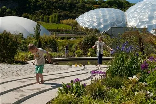 Двое маленьких детей играют в саду вокруг огромных куполов в Eden Project, Корнуолл.