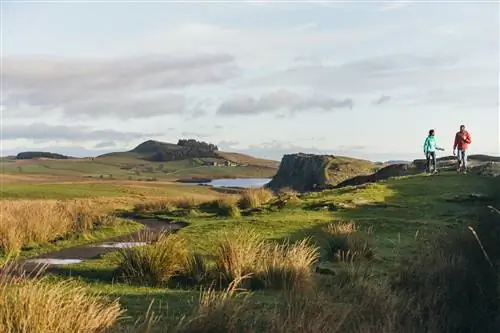 Двое туристов пересекают суровый ландшафт Нортумберлендских холмов.