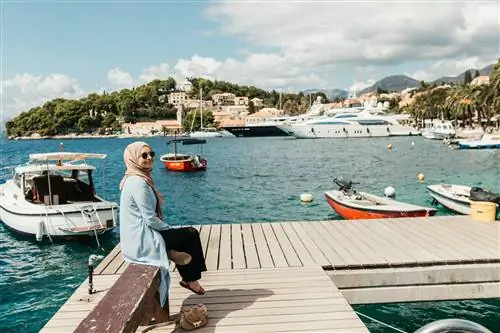 Женщина сидит на причале в солнечный день, а за ней лодки в воде.