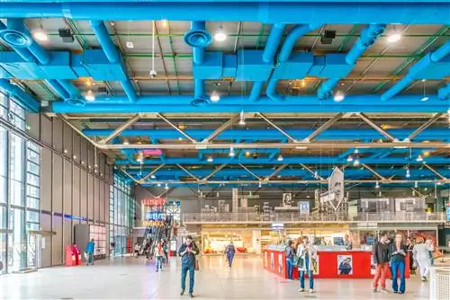 Люди ходят по ультрасовременному интерьеру музея с синей крышей.