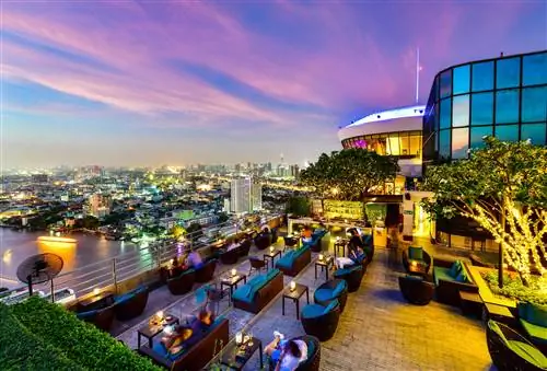 Ресторан-бар в сумерках с видом на городской пейзаж Бангкока, включая реку, в лаундже Three Sixty Lounge отеля Millennium Hilton Bangkok в Бангкоке, Таиланд.
