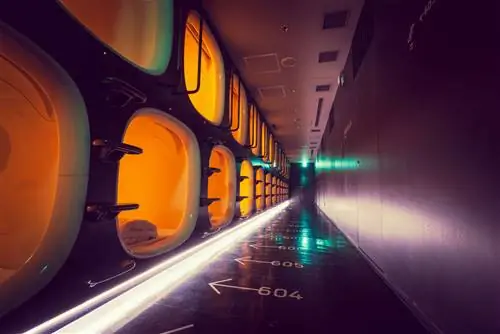 Освещенный неоновым светом коридор с двумя уровнями спальных капсул вдоль одной стены