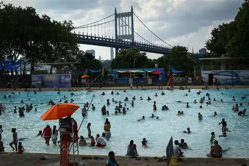 Люди наслаждаются теплым днем в бассейне Astoria Park Pool в Нью-Йорке, на фоне которого виден мост RFK.