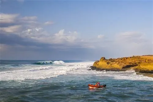 Двое мужчин в красной моторной лодке направляются к прибою на пляже Уалидия.