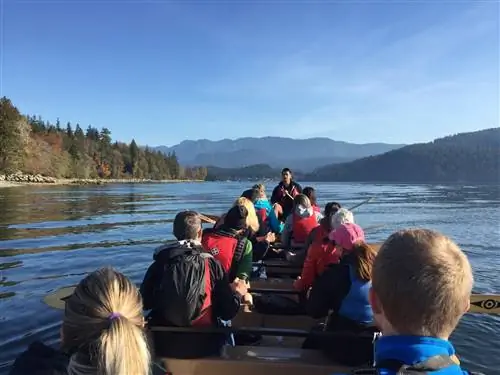 На каноэ несколько рядов гребцов плывут по спокойным водам Британской Колумбии.