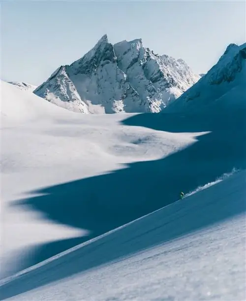 Вертикальное изображение лыжника, спускающегося с очень крутой снежной горы